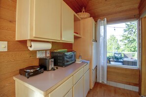 A compact kitchen with wooden cabinets, a toaster, a microwave, and a basket on the counter. - 4-Unit Group Retreat! 2 Hot Tubs & Walk to Beach (Hansville)