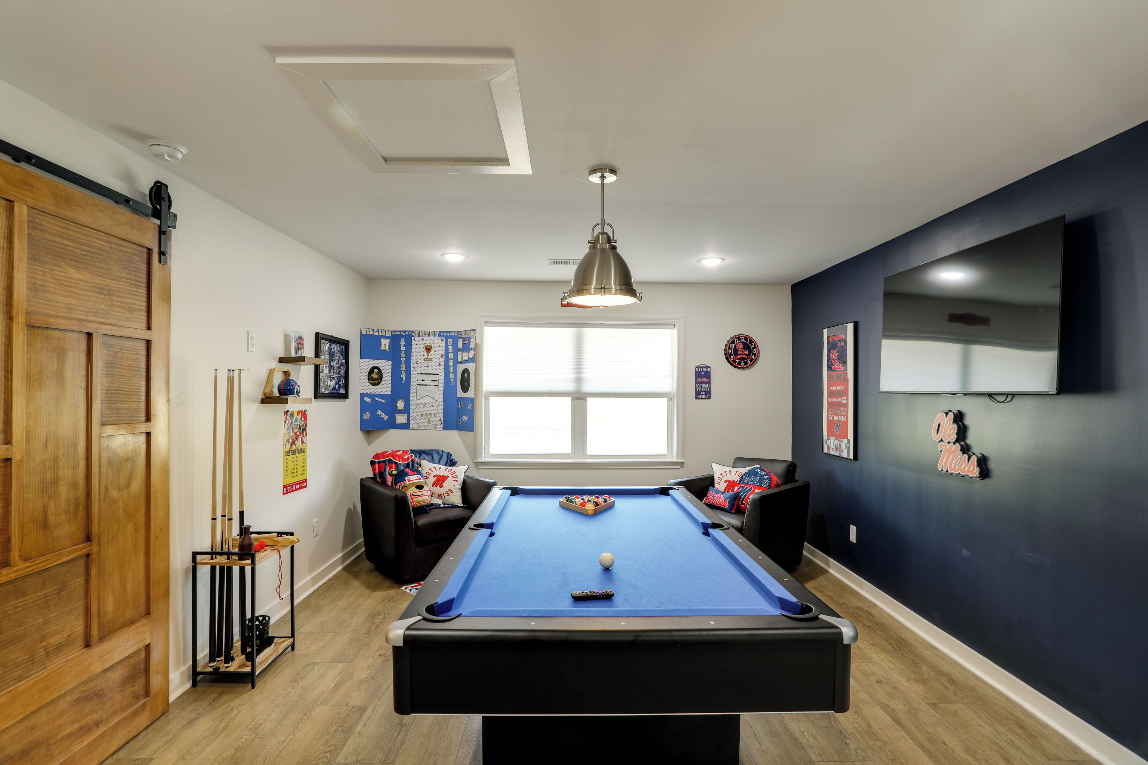 Une table de billard dans une pièce dont un mur est peint en bleu foncé, avec une fenêtre et divers objets de collection liés au sport.