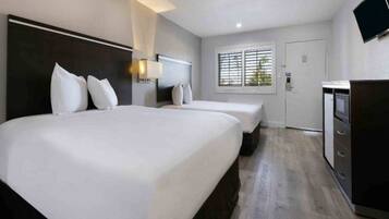 A hotel room with two beds, a TV, and a desk.