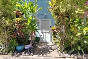 A gated entrance with a stone pathway leading to a white door, surrounded by lush tropical plants. - Welcome to Paradise, Perfect Getaway (Kihei)