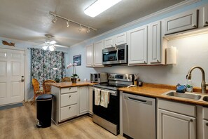 A kitchen with white cabinets, stainless steel appliances, a ceiling fan, and a window with a view of the outdoors. - Welcome to Paradise, Perfect Getaway (Kihei)