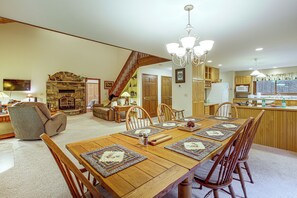 A spacious living area with a fireplace, dining table with placemats, and a kitchen with wooden cabinets. - Northwoods Home on a Private No-Motor Lake (Lakewood)