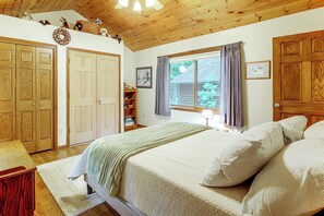 A bedroom with a bed, a window with curtains, a wooden ceiling, and a door. - Northwoods Home on a Private No-Motor Lake (Lakewood)