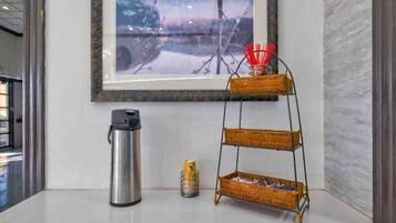 A framed artwork on the wall, a stainless steel thermos, a stack of cans, and a three-tiered wicker shelf with red straws.