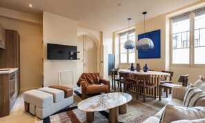 A modern living room with a flat-screen TV, a dining area with a table and chairs, and a sofa set. - CHIC 3-BEDROOM PARISIAN RETREAT NEAR THE PICASSO MUSEUM (Paris)