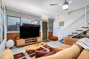Ein modernes Wohnzimmer mit Flachbildfernseher, einer Couch, einem Couchtisch und einer Treppe.