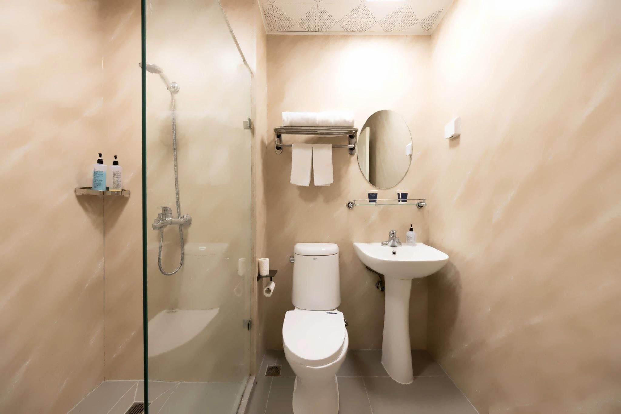 A bathroom with a glass shower enclosure, a toilet, a sink, and a mirror.