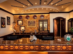 A hotel reception area with a marble counter, framed artwork, clocks, and a sign for the Petra Canyon Hotel. - Petra Canyon Hotel Petra (Wadi Musa)