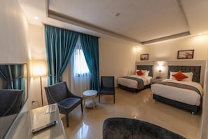Habitació d'hotel amb dos llits, un escriptori, una cadira, una taula petita i una finestra amb cortines.