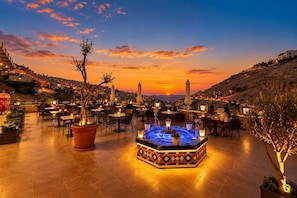 An outdoor dining area with tables and chairs, a central decorative fountain, and a sunset view. - Petra Canyon Hotel Petra (Wadi Musa)