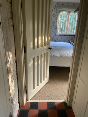 Un pasillo estrecho que conduce a un dormitorio con cama, ventana de diseño floral y suelo a cuadros.