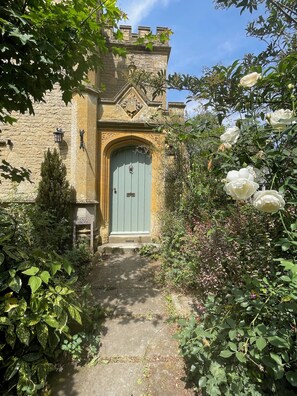 A stone building with a blue door, surrounded by lush greenery and white flowers.
