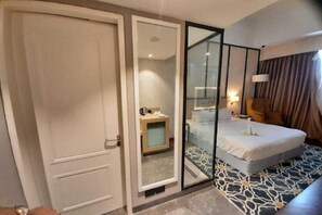 Una habitación de hotel con cama, mesita de noche, espejo y un escritorio pequeño con silla.
