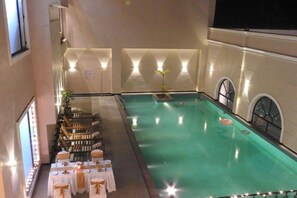 An indoor swimming pool with a seating area and tables, surrounded by walls with light fixtures. - Polo Hotels, Agartala (Agartala)