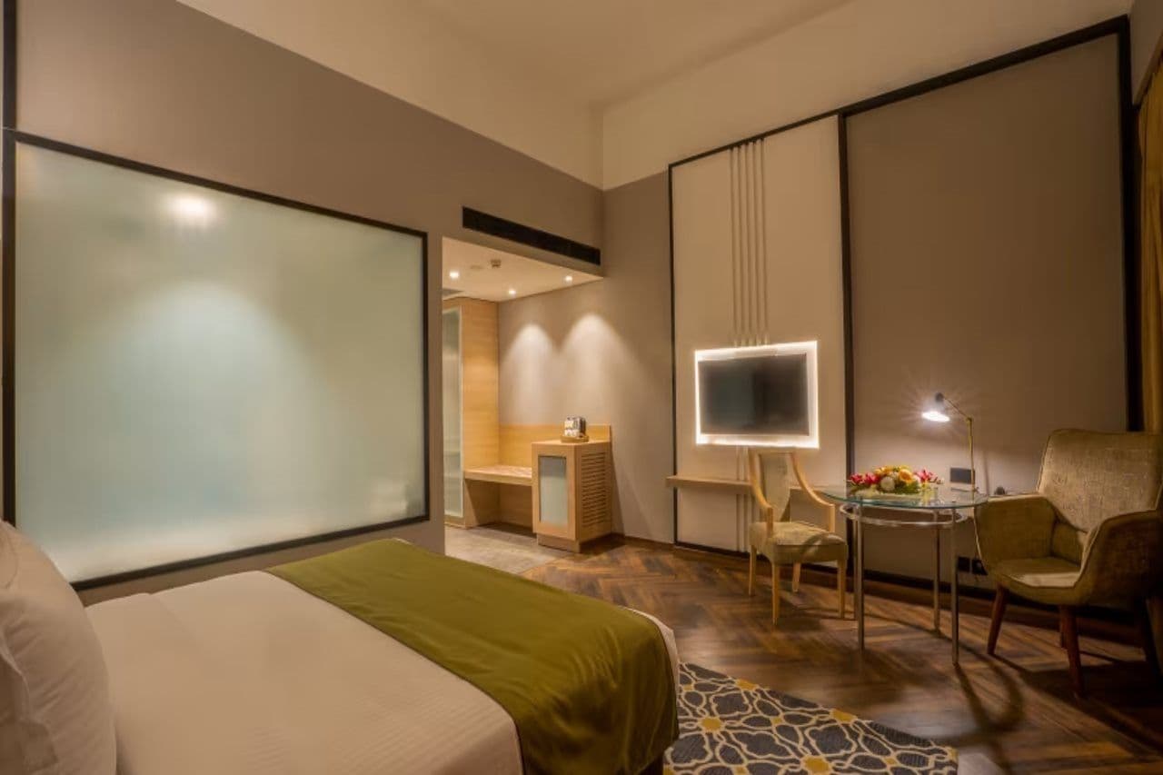 A hotel room with a bed, a desk with a computer, a chair, and a television.