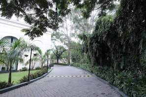 A paved pathway flanked by lush greenery and a white building with a curved facade. - Polo Hotels, Agartala (Agartala)