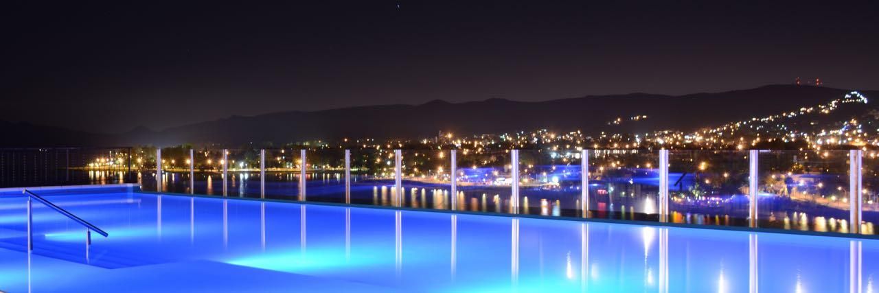 Une vue nocturne d’une piscine, avec une vue sur la ville en arrière-plan.