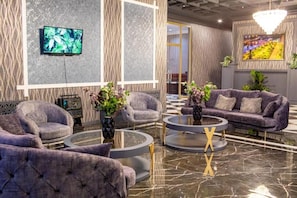 A modern lobby with a marble floor, grey upholstered sofas, and a television mounted on the wall. - Volga Hotel Baku (Baku)
