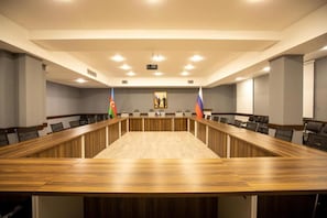 A conference room with a long table, chairs, flags, and a projector screen. - Volga Hotel Baku (Baku)