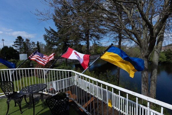A balcony with a white railing, a table, and chairs. Flags of the USA, Canada, and Ukraine are displayed. - Killarney View House (Killarney)
