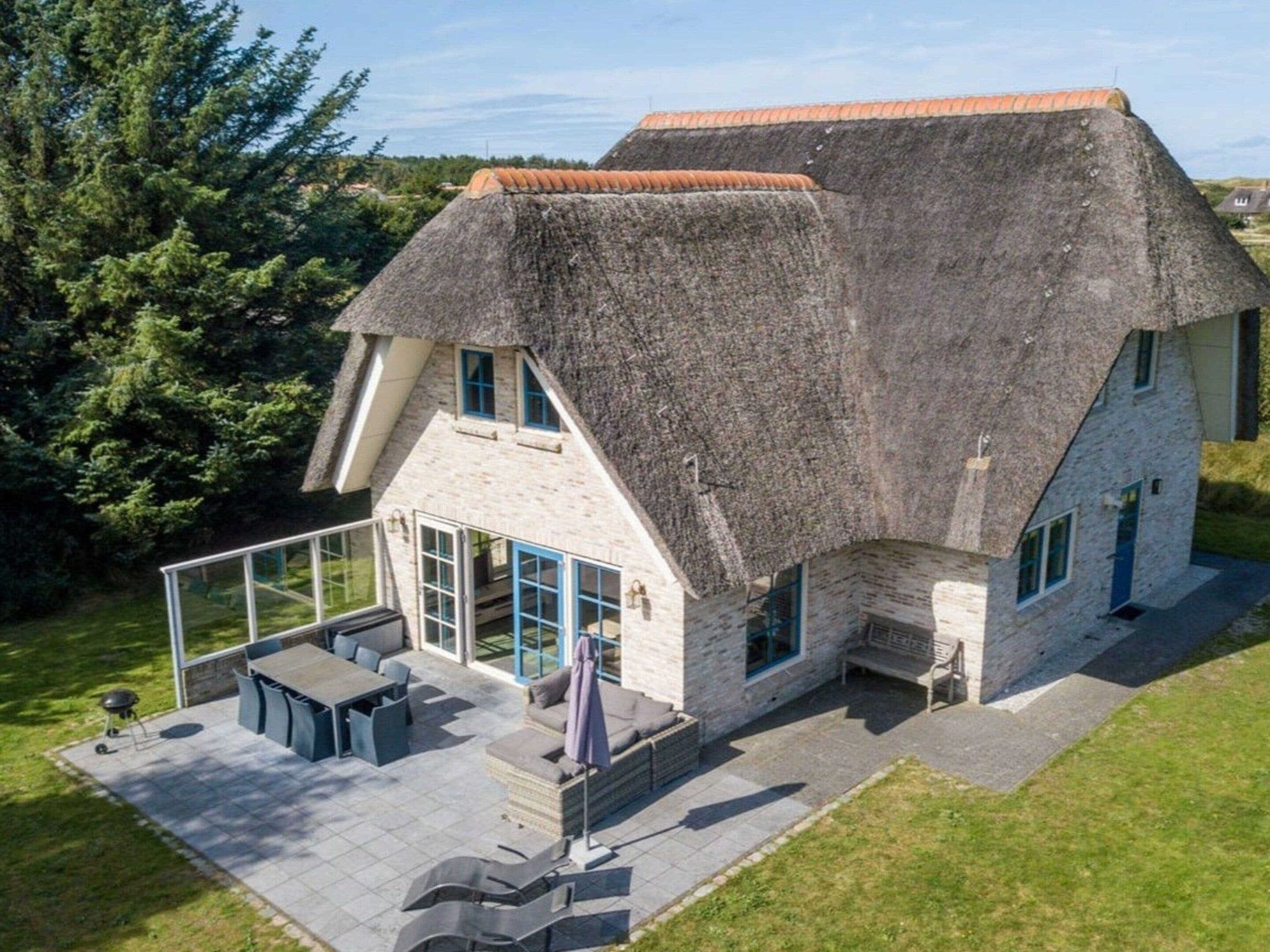 A thatched-roof house with a patio area, outdoor seating, and a view of the surrounding landscape.