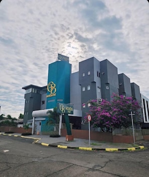 Un hotel amb una façana destacada de color blau i gris, un senyal que indica 'HOTELES Foz' i una zona d'aparcament amb vorades grogues.