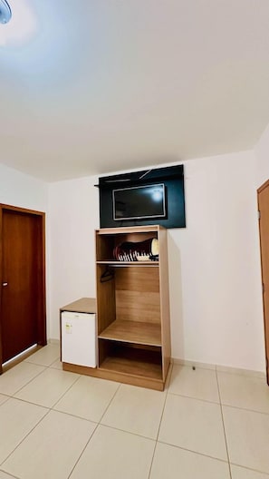 Habitació amb un armari de fusta, un petit moble blanc i un televisor penjat.