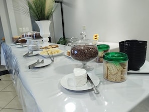 Taula de buffet amb diversos aliments, incloent un recipient de vidre amb xips de xocolata, un plat amb formatge blanc i pots de pickles i galetes.