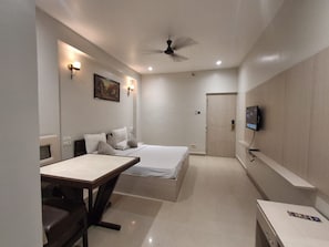 A compact hotel room with a bed, a desk, a chair, a television, and a ceiling fan. - Hotel Downtown (Rajkishore Nagar)