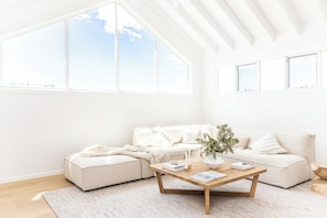 Ein modernes Wohnzimmer mit großem Fenster, einem weißen Sofa, einem Couchtisch und einer Pflanze.