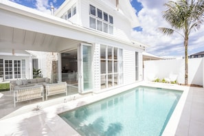 Ein modernes, zweistöckiges Haus mit Pool, großen Fenstern und einer überdachten Terrasse.