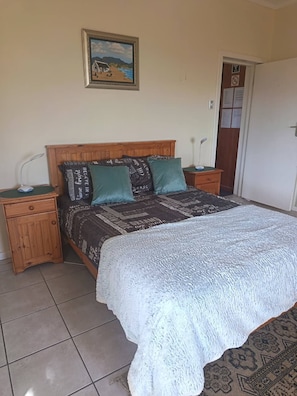 A bedroom with a bed, two bedside tables, a nightstand, a framed picture on the wall, and a door with a sign. - Mountain Side Golden gem (Cape Town)