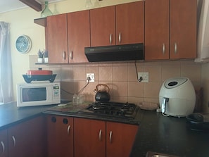 A kitchen with wooden cabinets, a microwave, a kettle, and a coffee maker. - Mountain Side Golden gem (Cape Town)