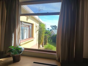 A window with curtains, a potted plant, and a view of a house and greenery outside. - Mountain Side Golden gem (Cape Town)