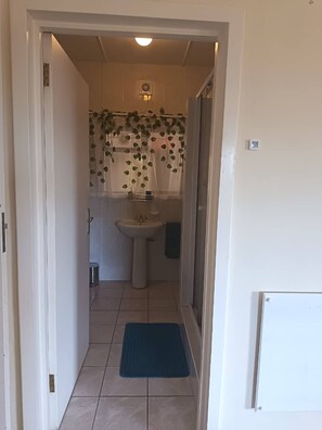 En smal hall leder till ett badrum med handfat, toalett och duschdraperi med lövmönster.