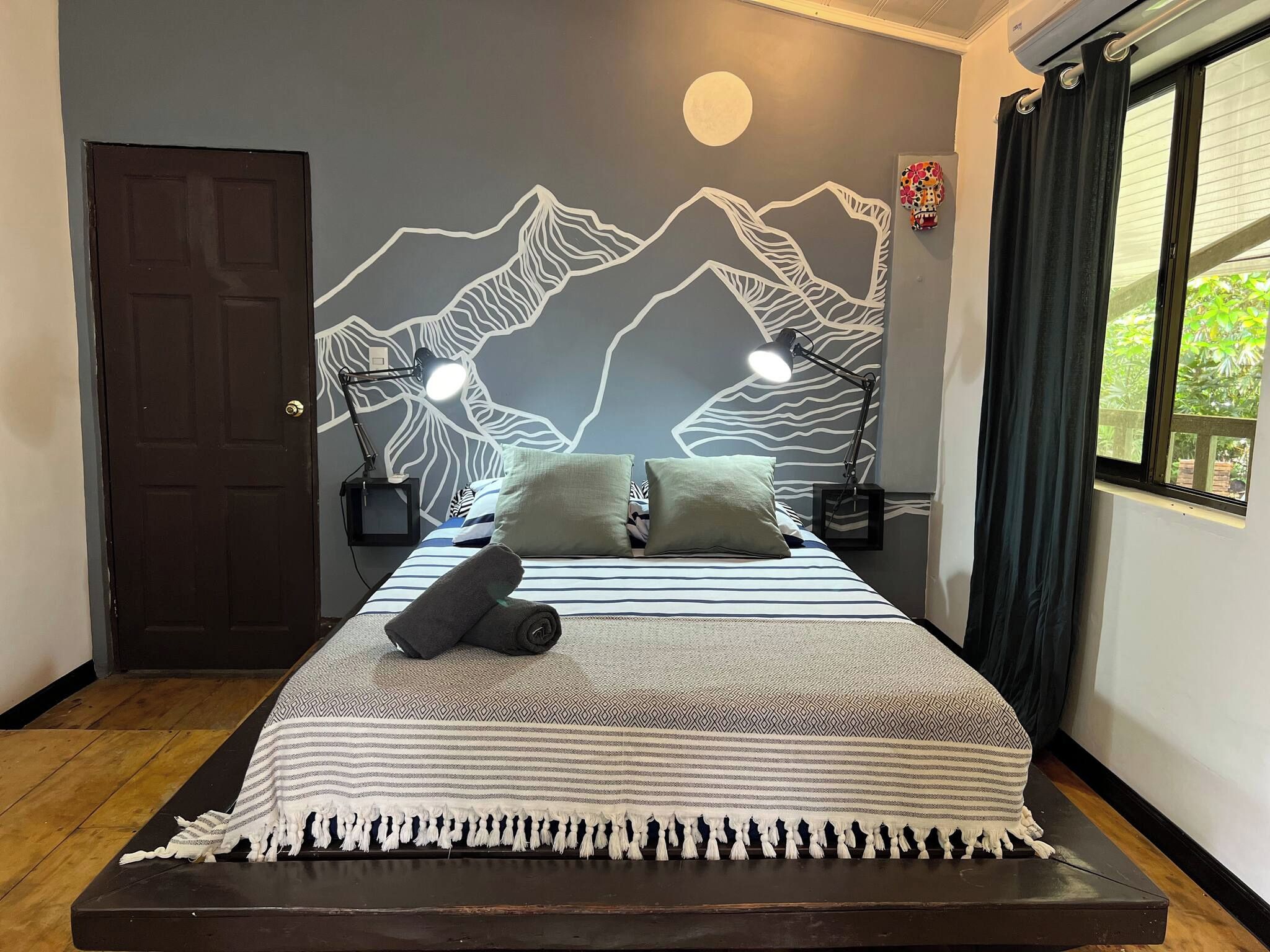 Ein Bett mit einem gemusterten Bettüberwurf, zwei Kissen, ein gerolltes Handtuch und zwei Nachttischlampen.