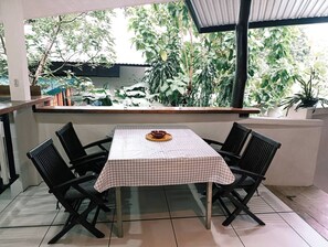 Een eetgedeelte met een tafel voor vier personen, omringd door stoelen, met uitzicht op weelderige begroeiing door een raam.