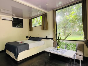 A hotel room with a bed, a small table, a chair, a window with curtains, and a plant. - Private Jungle Box in Playa Cocles (Puerto Viejo de Talamanca)