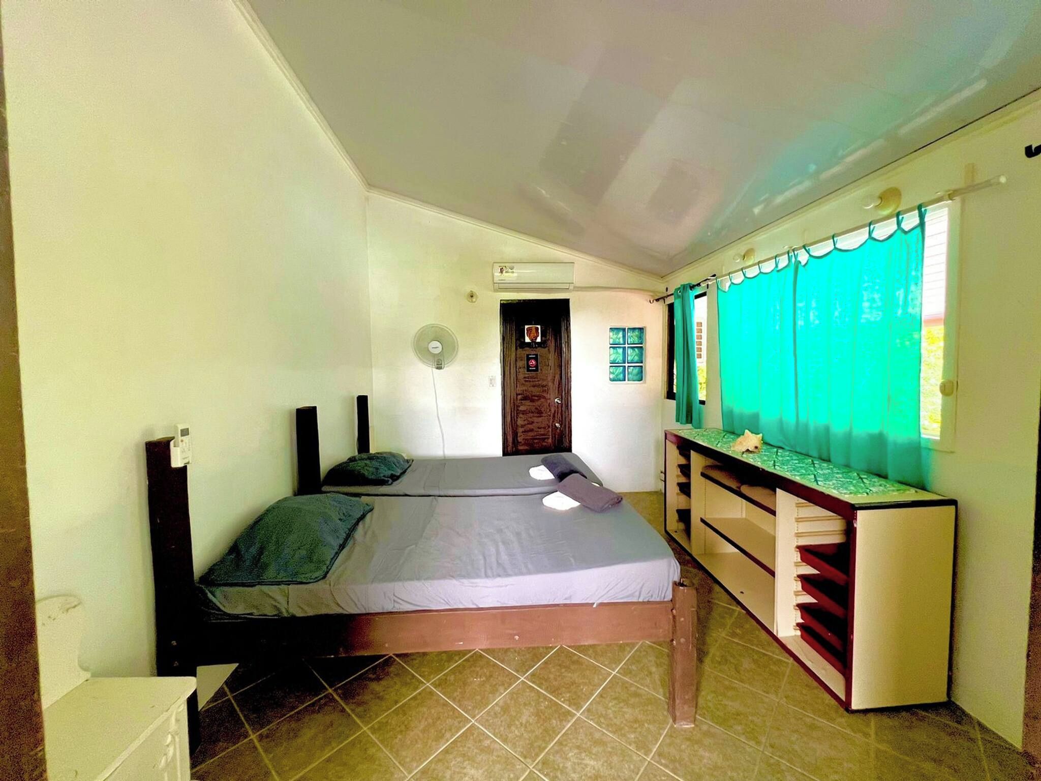 A room with a bed, a desk, a chair, a window with curtains, and an air conditioning unit.