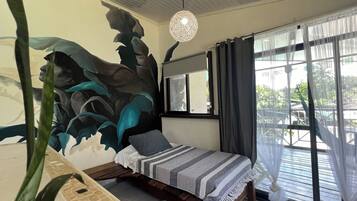 Une chambre à coucher avec un lit, une grande fenêtre avec des rideaux, un luminaire suspendu et une fresque murale.
