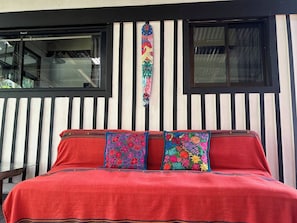 Una cama con una cubierta roja y dos almohadas coloridas, frente a una pared con rayas verticales negras y blancas.