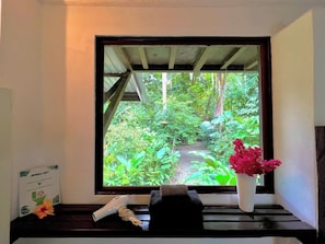 Une fenêtre donnant sur un jardin luxuriant, un vase blanc rempli de fleurs et une enseigne indiquant « Jungle Loft ».