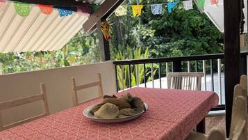 Ein Balkon mit einem Tisch für zwei Personen, einer rot gemusterten Tischdecke und einem Teller Essen.