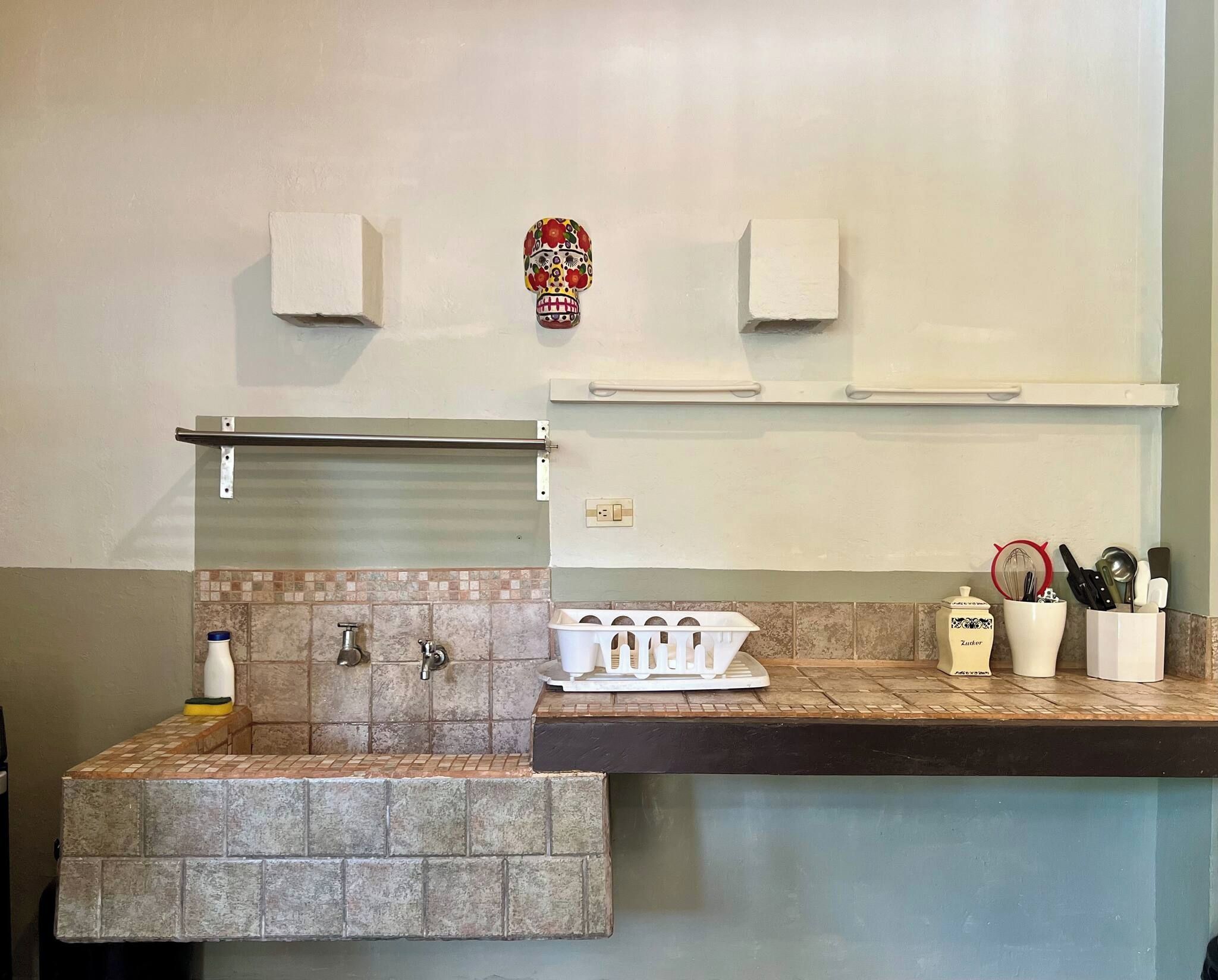 A bathroom with a sink, two faucets, a mirror, a towel rack, and a decorative mask on the wall.