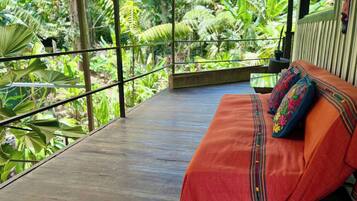 Une terrasse en bois avec un banc et des coussins aux couleurs vives, entourée d’une végétation tropicale luxuriante.
