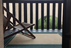 A room with a wooden chair, a patterned mat, and a view of greenery through a black and white striped railing. - Affitto camere con servizi bagno privati, in villa con giardino in luogo di pace (Sandrà)