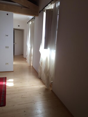 A hallway with wooden flooring, white walls, and a door at the end. - Affitto camere con servizi bagno privati, in villa con giardino in luogo di pace (Sandrà)