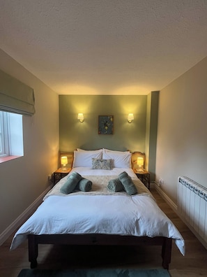 A neatly made bed with pillows and a blanket, two bedside lamps, a small table with a lamp, and a painting on the wall. - Cozy Holiday Retreat in Bradford Abbas - Modern Comfort Awaits (Sherborne)