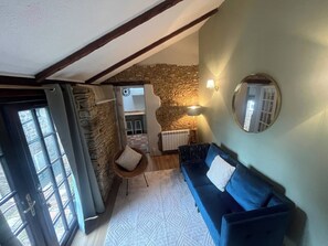 A room with a stone wall, a blue sofa, a round mirror, and a window with a view. - Cozy Holiday Retreat in Bradford Abbas - Modern Comfort Awaits (Sherborne)