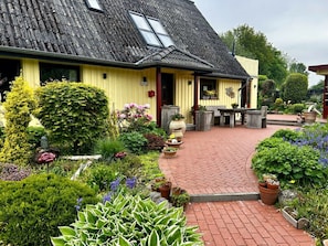A yellow building with a sloped roof and a brick pathway leading to a wooden bench area. - Holiday Apartment With 2 Bedrooms (Kappeln)